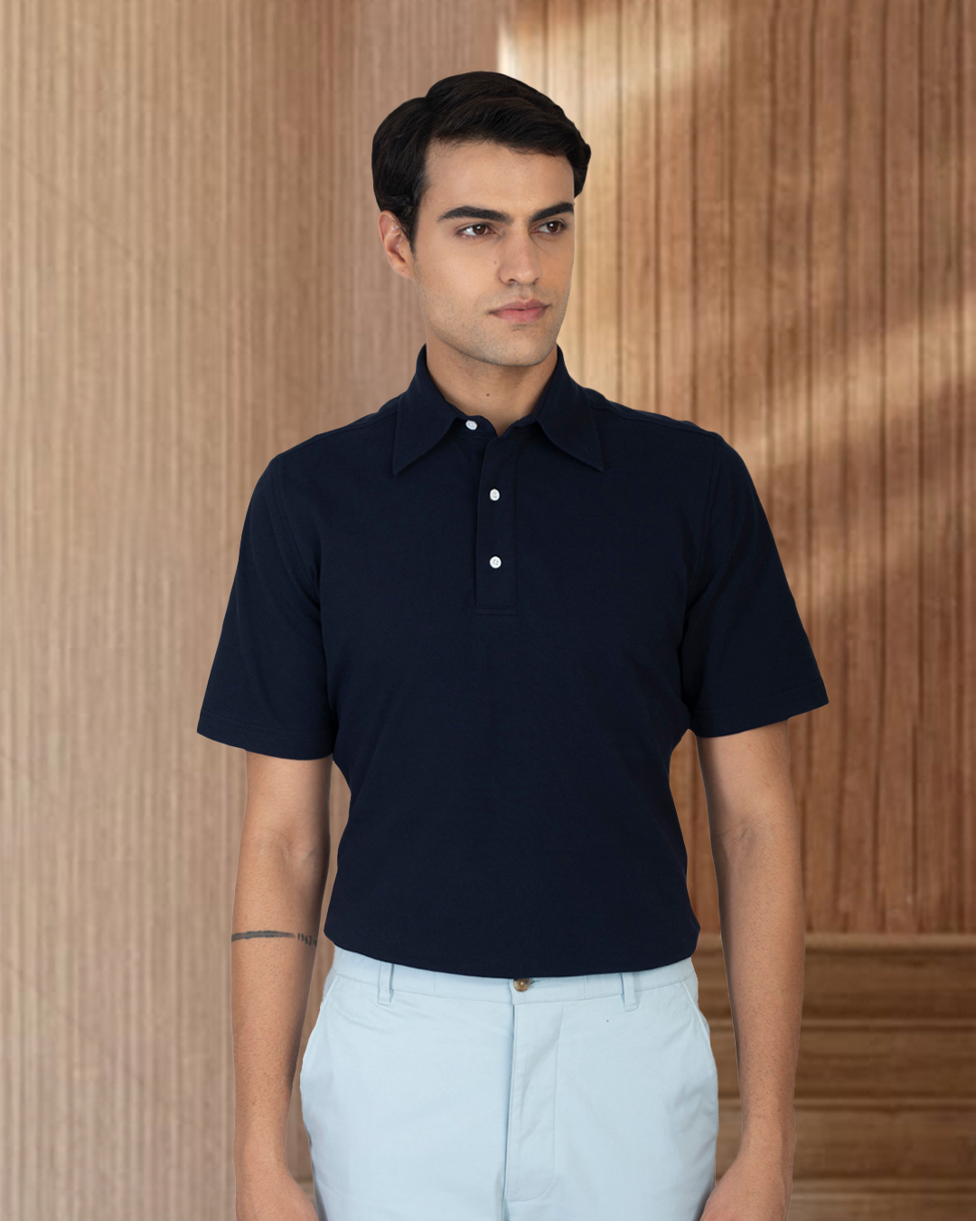 Model wearing the custom oxford polo shirt for men by Luxire in navy with white pants