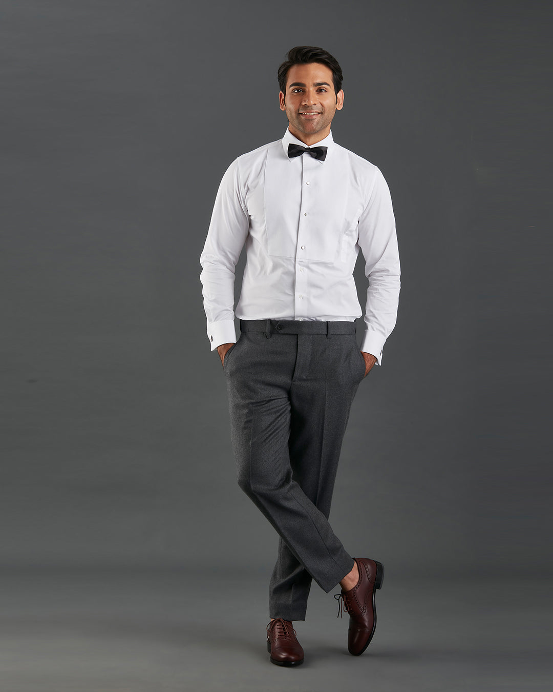 Model wearing mens tuxedo shirt by Luxire in white with black bow tie hands in pockets 2