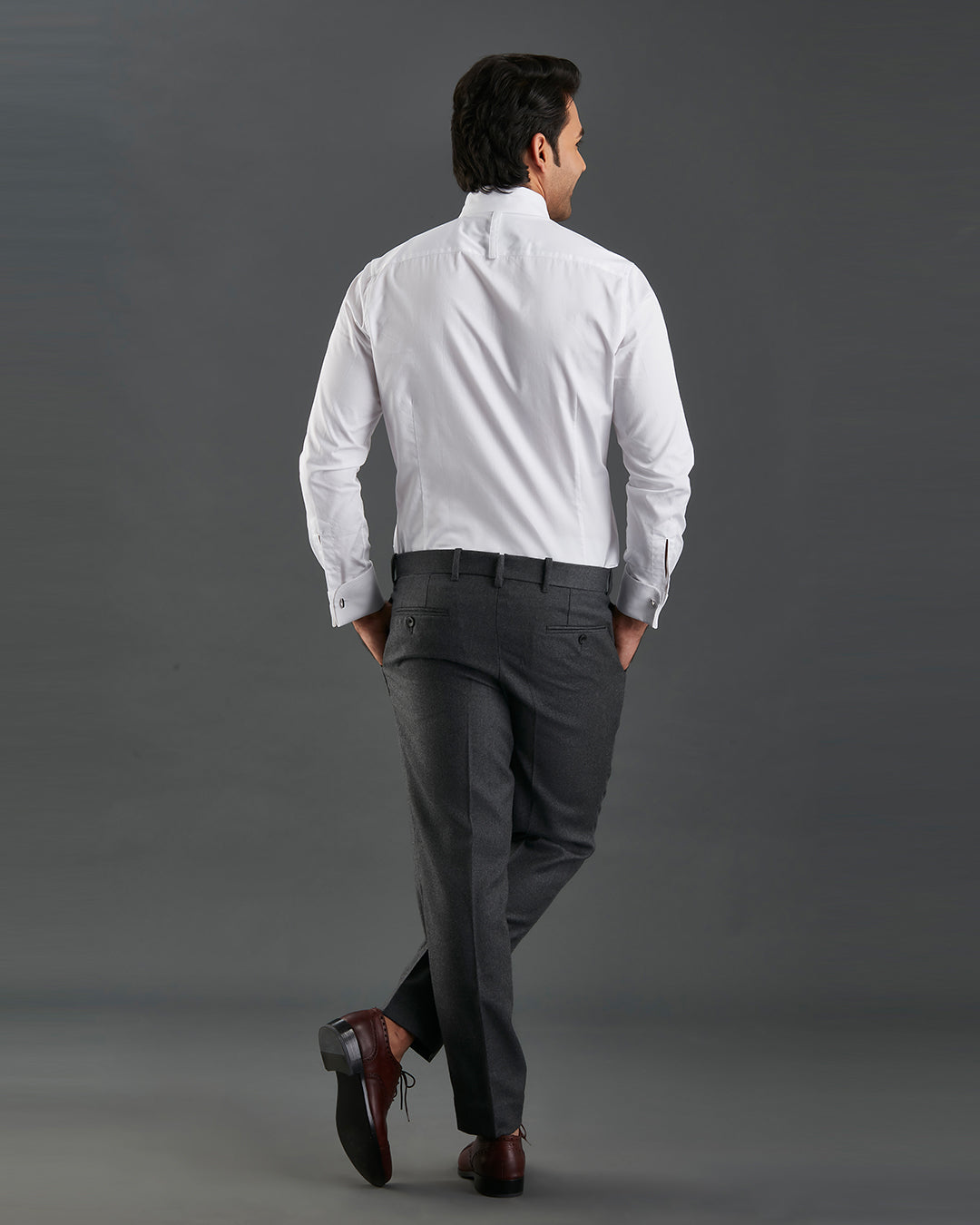 Back of model wearing mens tuxedo shirt by Luxire in white with black bow tie hands in pockets